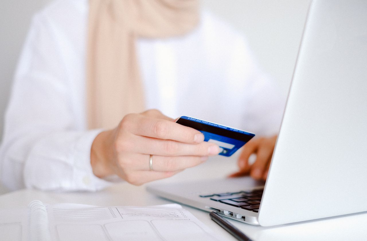 services-03 Close-up of a person holding a credit card while using a laptop for online shopping.