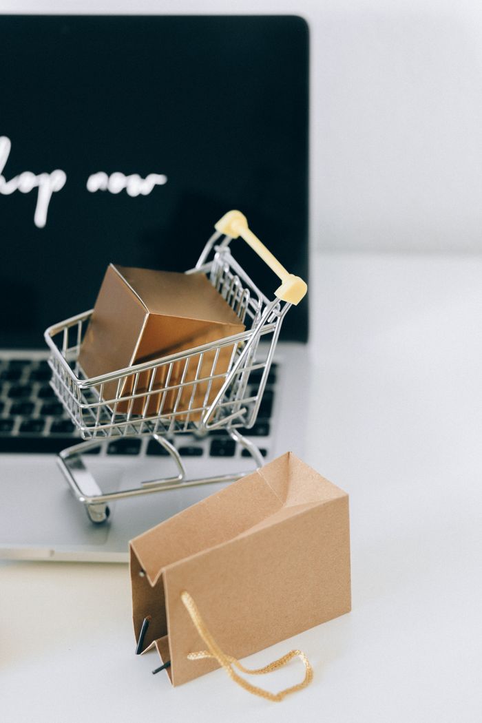 about-01 A miniature shopping cart with a parcel on a laptop symbolizes online shopping and e-commerce.